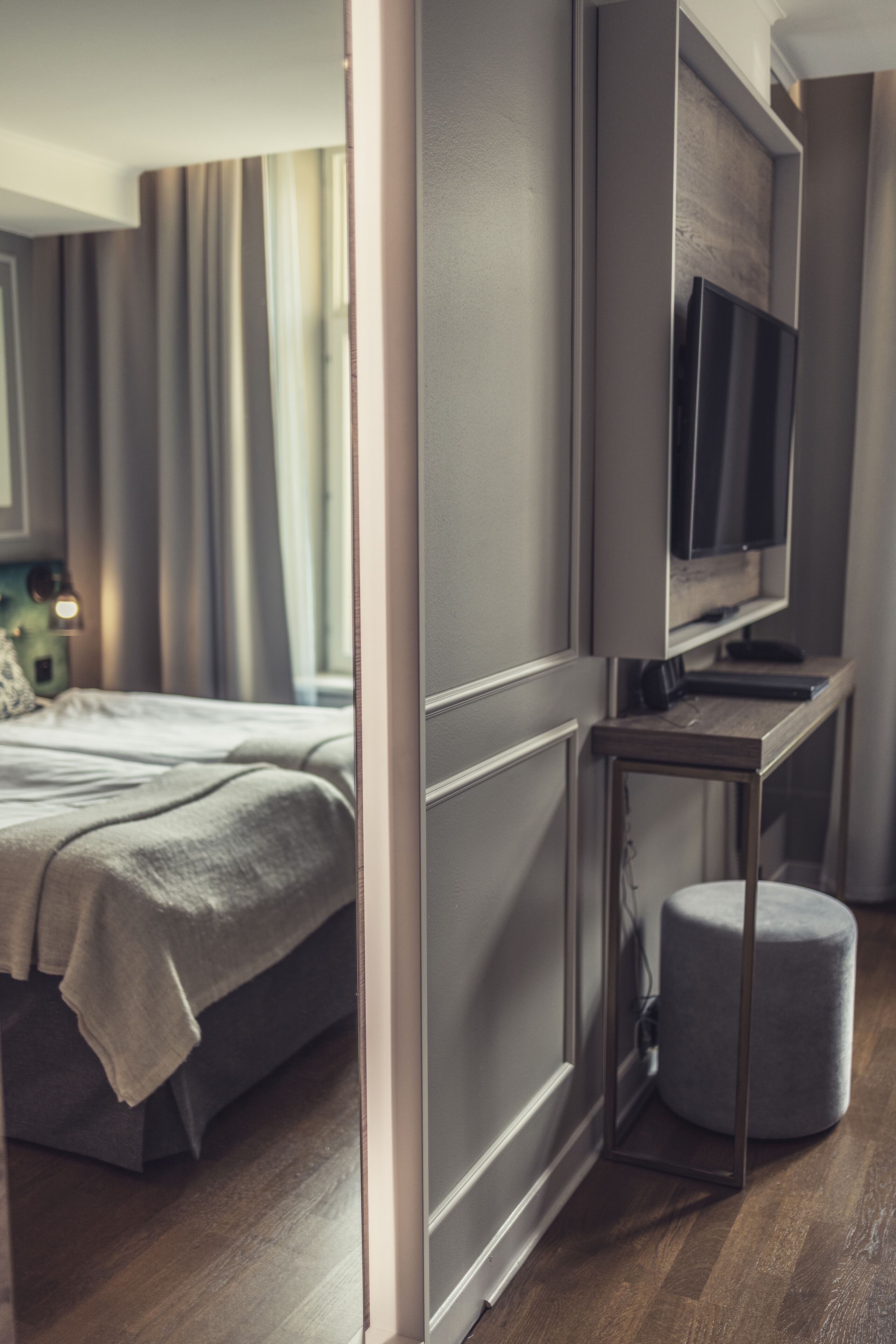 A modern bedroom with a bed, a TV on a stand, and a small ottoman.