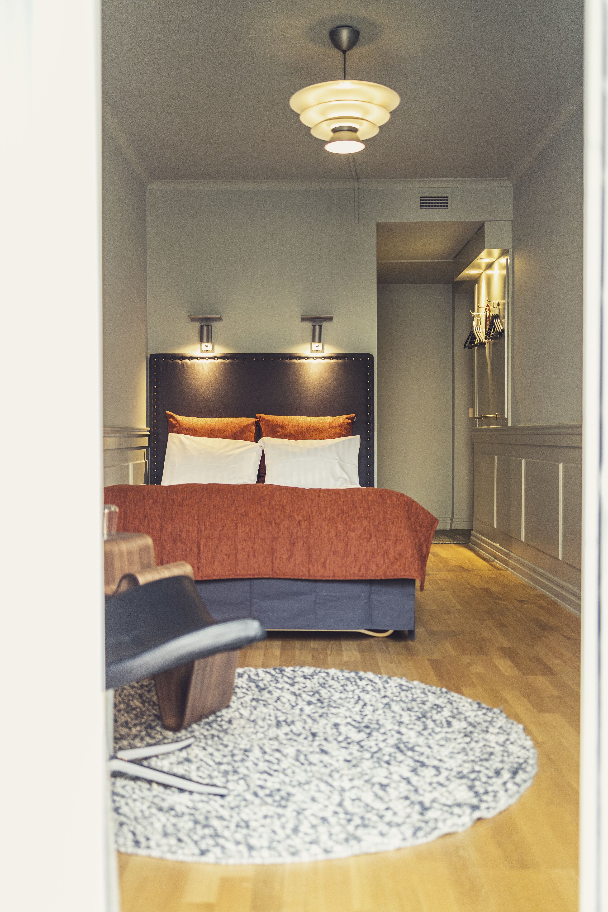 A bedroom with a bed, a round rug, a chair, and a ceiling light.