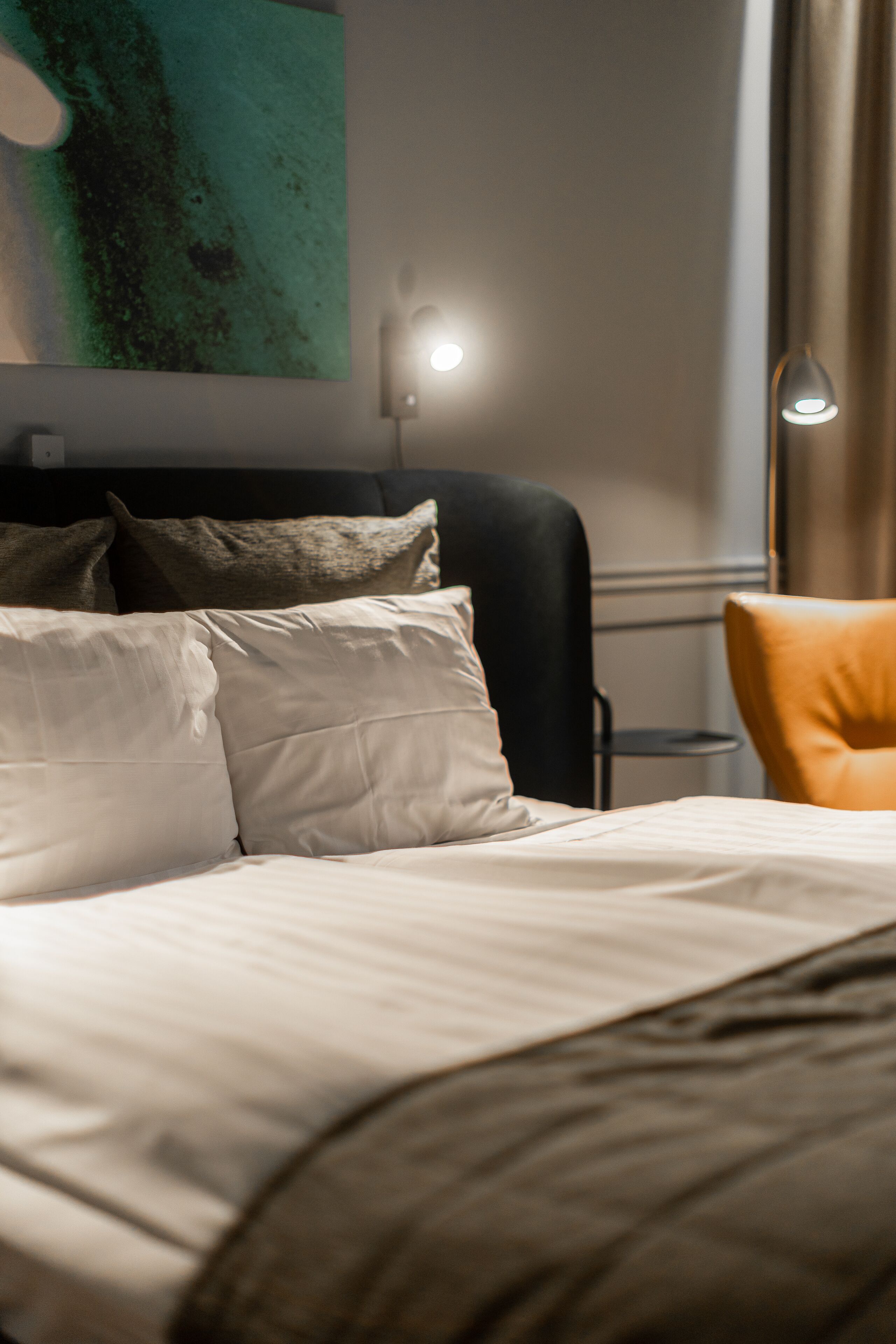 A neatly made bed with pillows, a black chair, and a lamp in a modern hotel room.