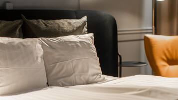 A neatly made bed with pillows, a black chair, and a lamp in a modern hotel room.