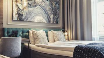 Et moderne hotelværelse med et stort abstrakt maleri på væggen, en polstret sengegavl, et natbord med et ur og udsigt til det fri gennem vinduet.