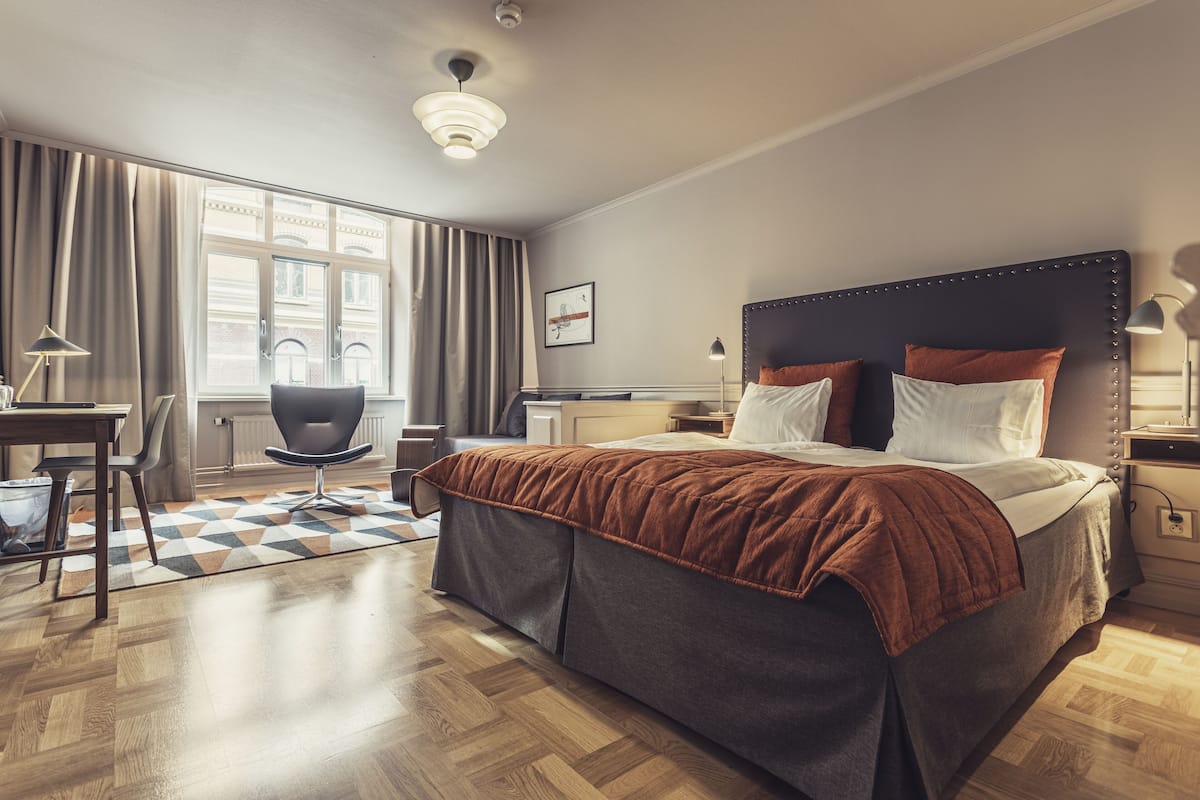 A hotel room with a large bed, a desk, a chair, and a view of the city through the window.