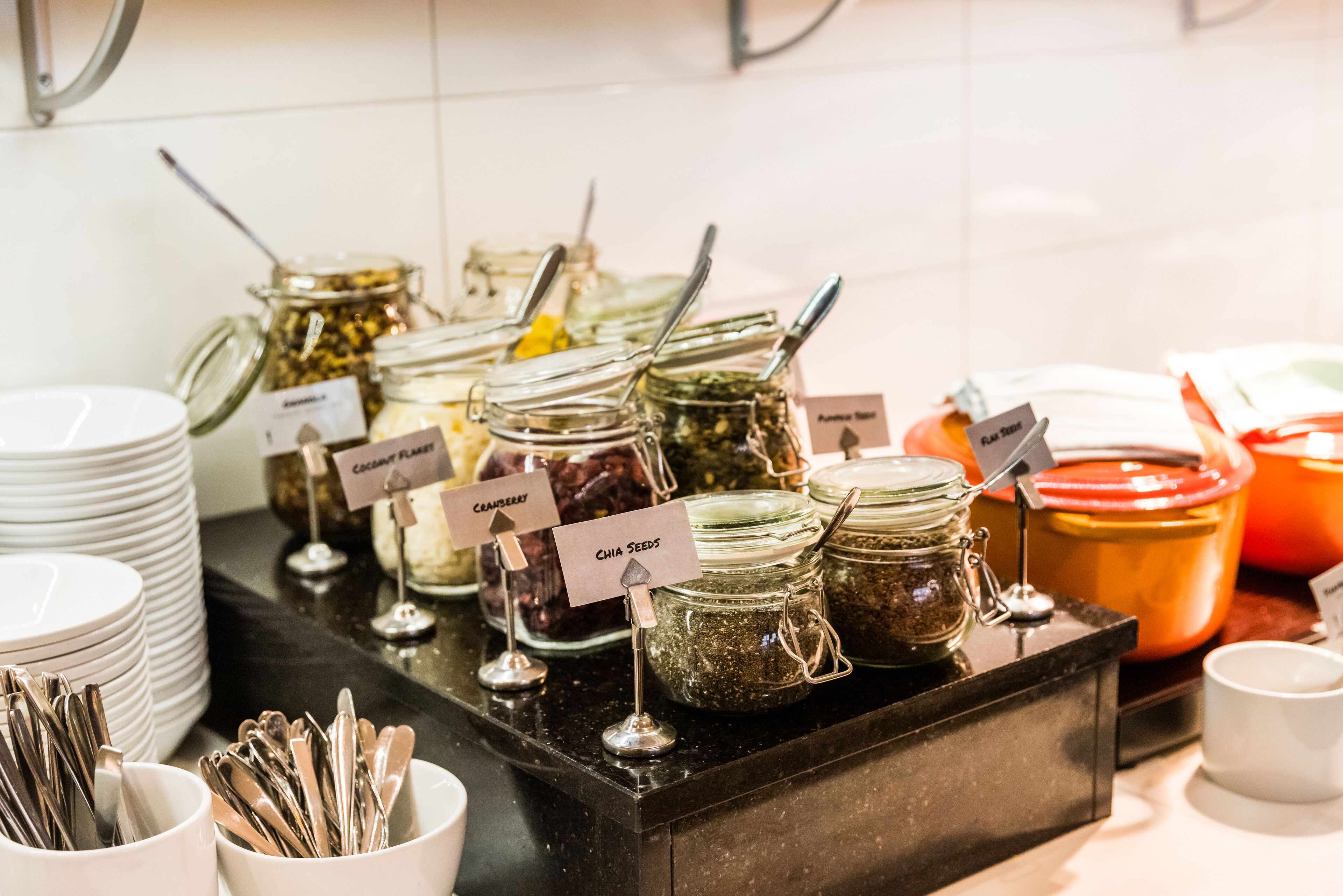 A buffet with labeled jars of food items such as cranberry and chia seeds.