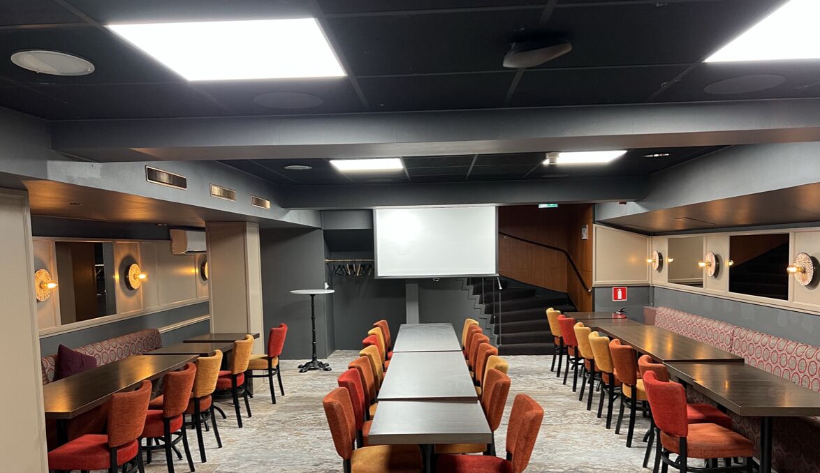 Une salle de conférence dotée d’une longue table et de nombreuses chaises, ainsi que d’un écran de projection et d’un escalier menant à un autre niveau.