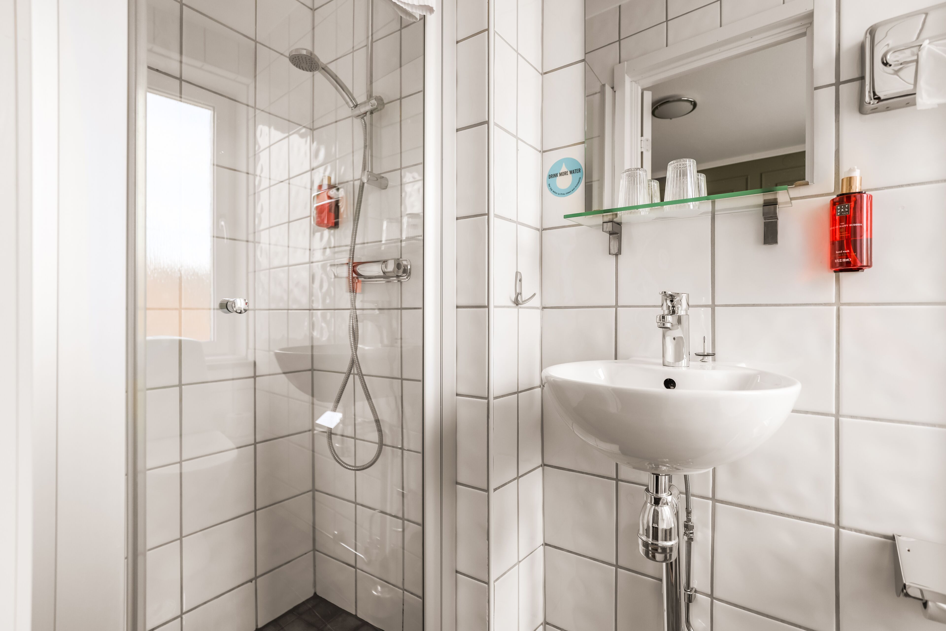 Une salle de bain moderne avec une douche à parois de verre, un lavabo blanc et un miroir au-dessus.