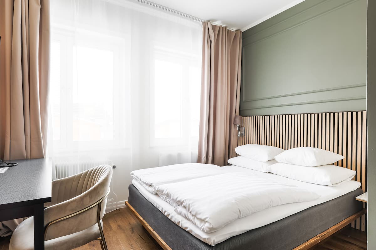 A hotel room with a bed, a desk, a chair, and a window with curtains.