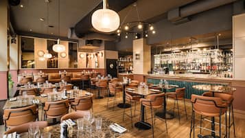 Ein Restaurant mit mehreren Tischen und Stühlen, einer Bar mit Flaschenregalen und Pendelleuchten.