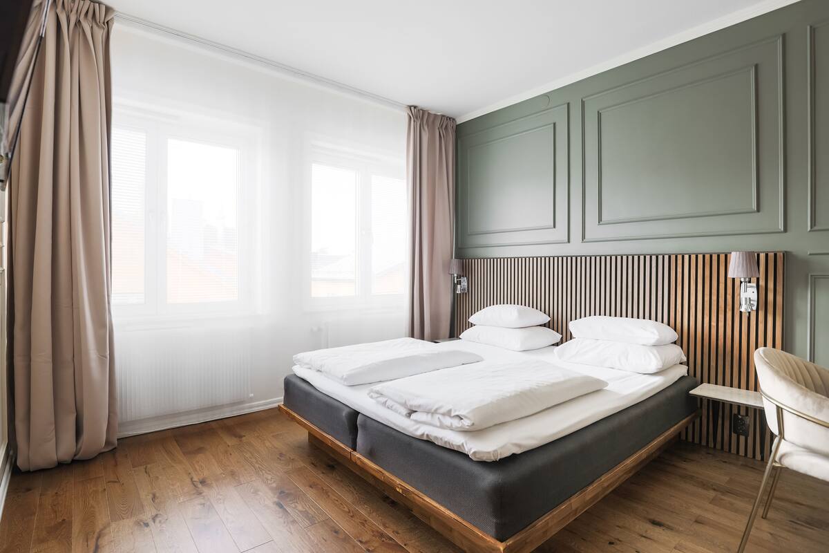 A modern bedroom with a wooden bed frame, a headboard with vertical slats, and a chair by the window.