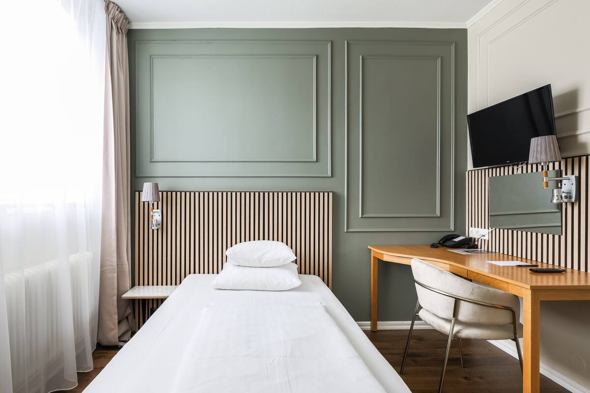 A hotel room with a bed, a desk, a chair, a TV, and a lamp.