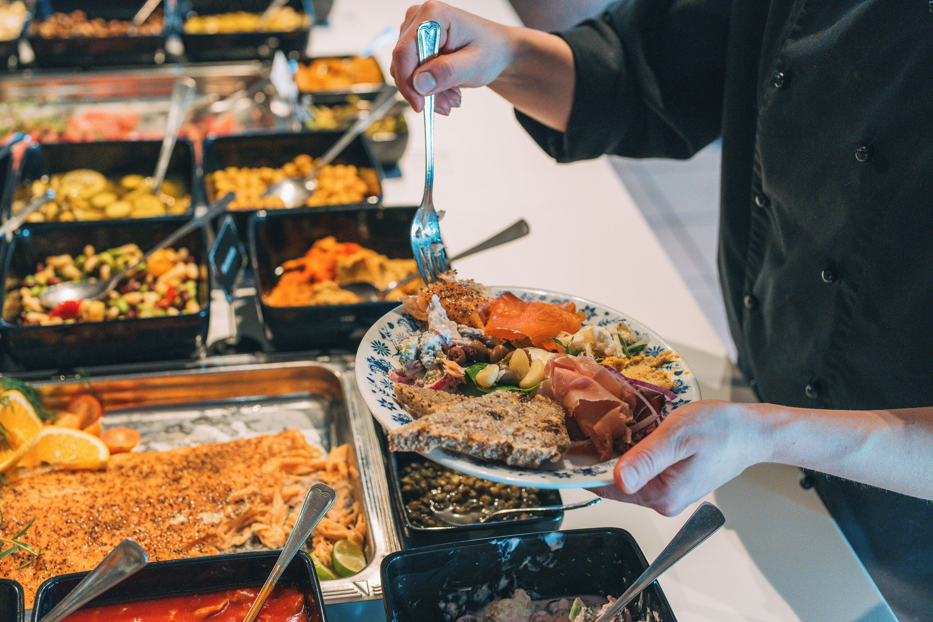 A buffet with various dishes and a person serving themselves.