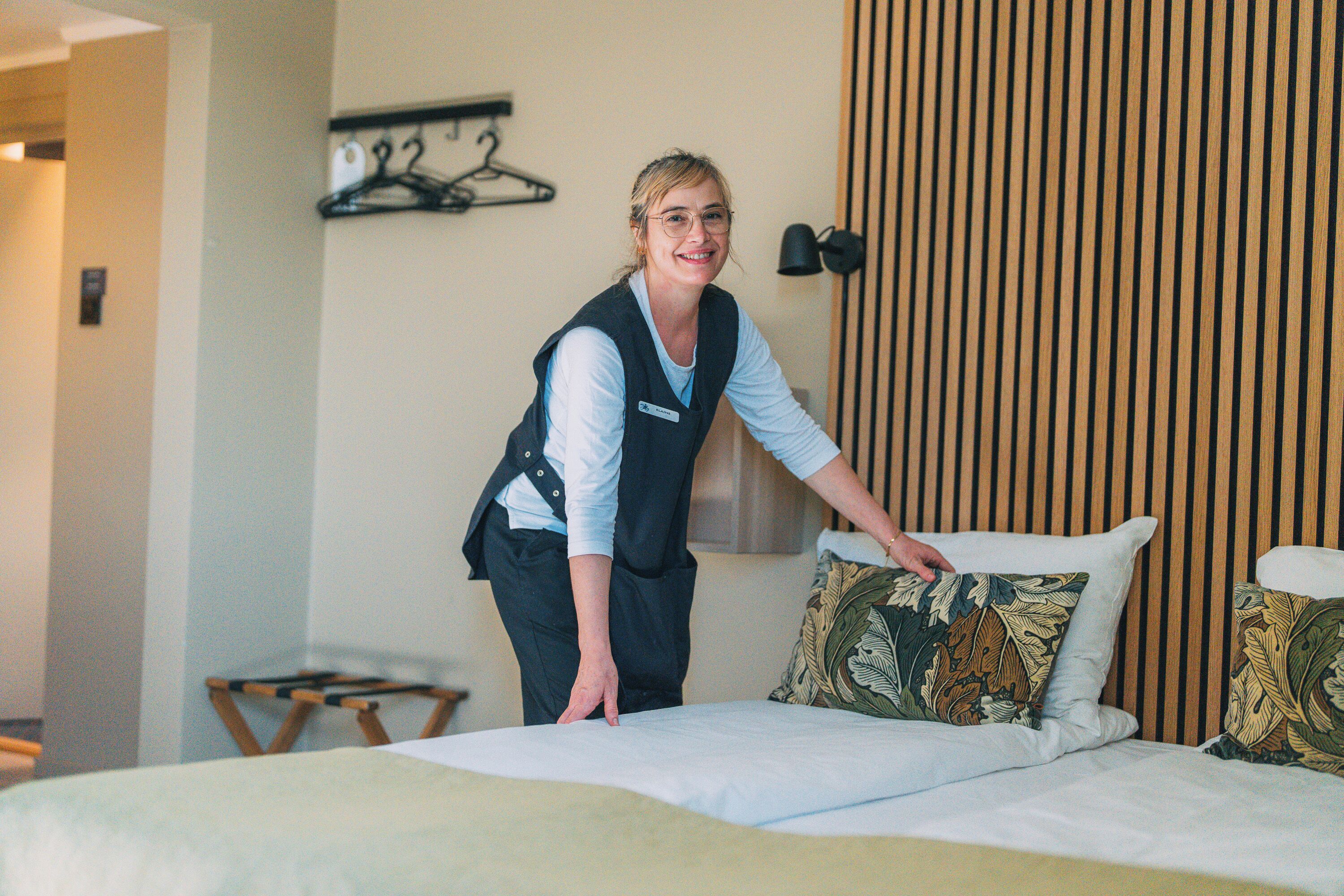A hotel room with a neatly made bed, a wooden headboard, and a small wooden chair.