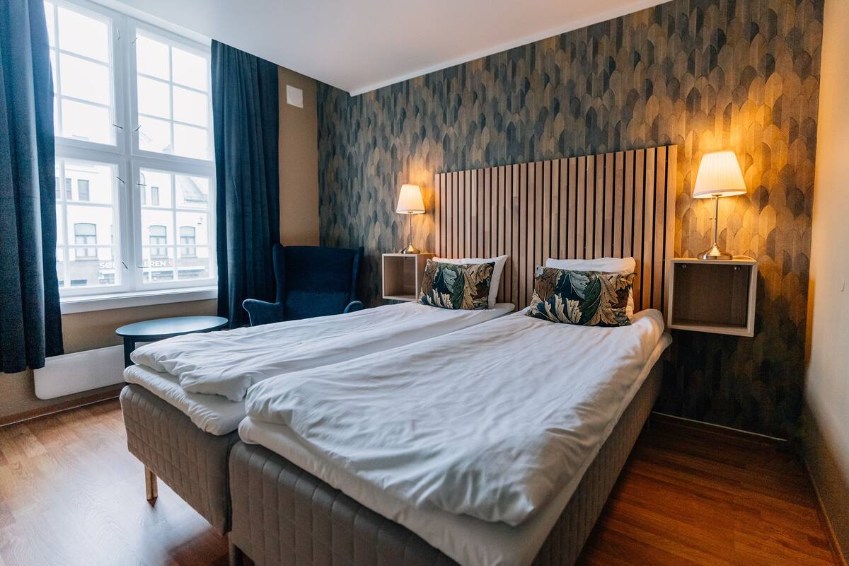 A hotel room with two beds, a round table, a chair, and a window with curtains.