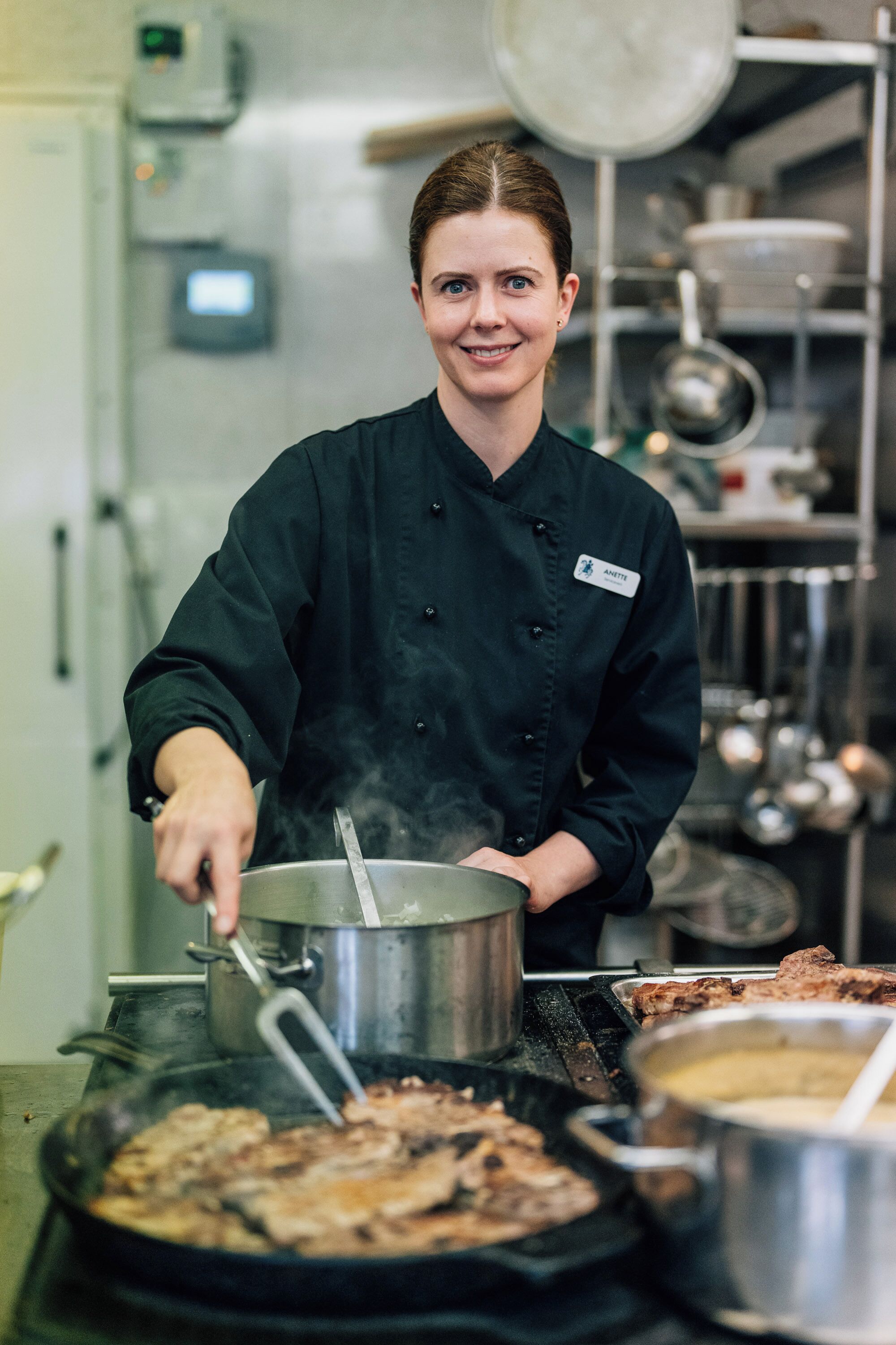 A chef in a professional kitchen with stainless steel equipment and a pot on a stove.