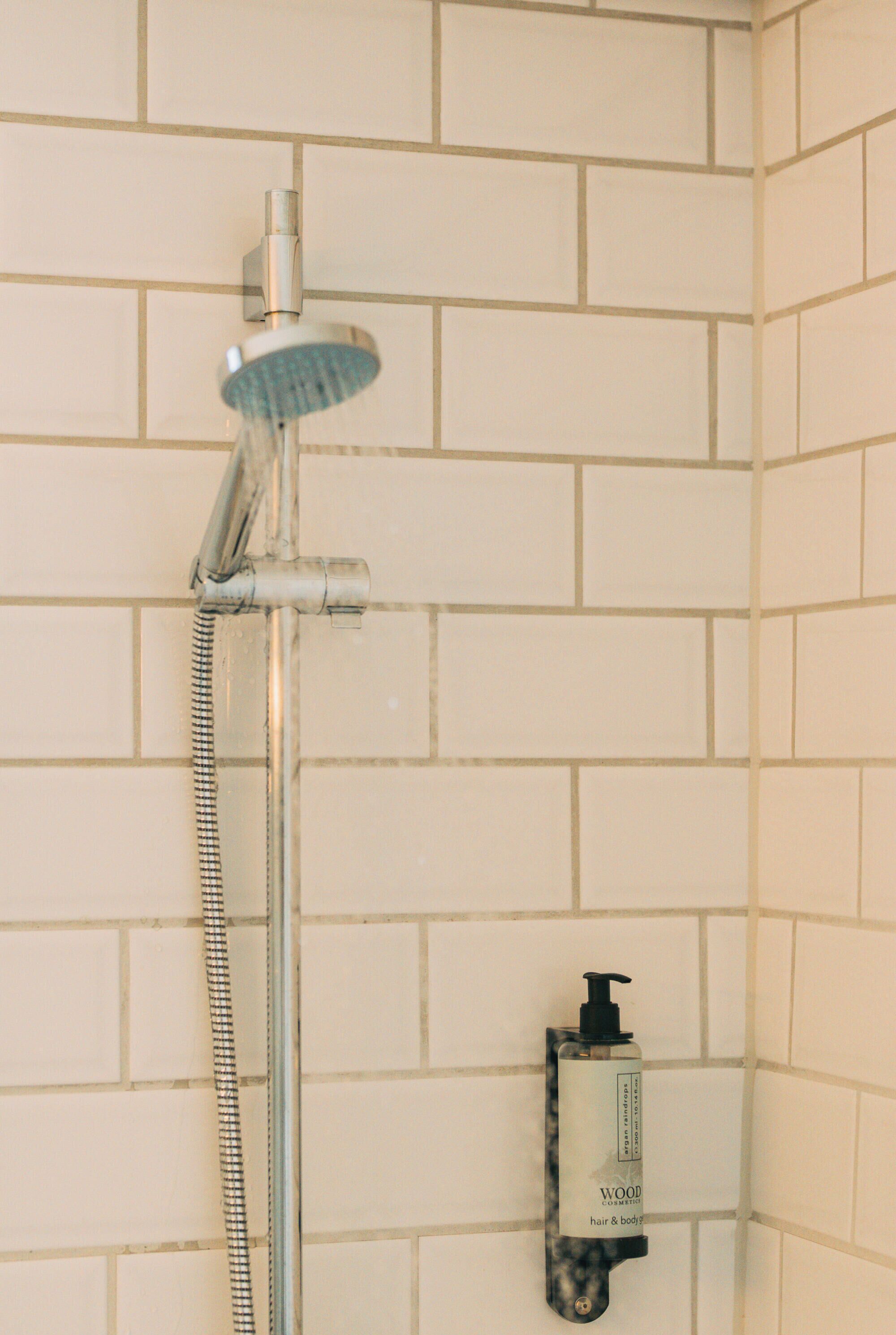 Ducha con cabezal de ducha de mano y dispensador de jabón de mano en una pared de azulejos.