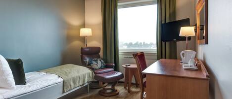 Una habitación de hotel con cama, una silla, un escritorio con cafetera, televisor y vista al exterior.