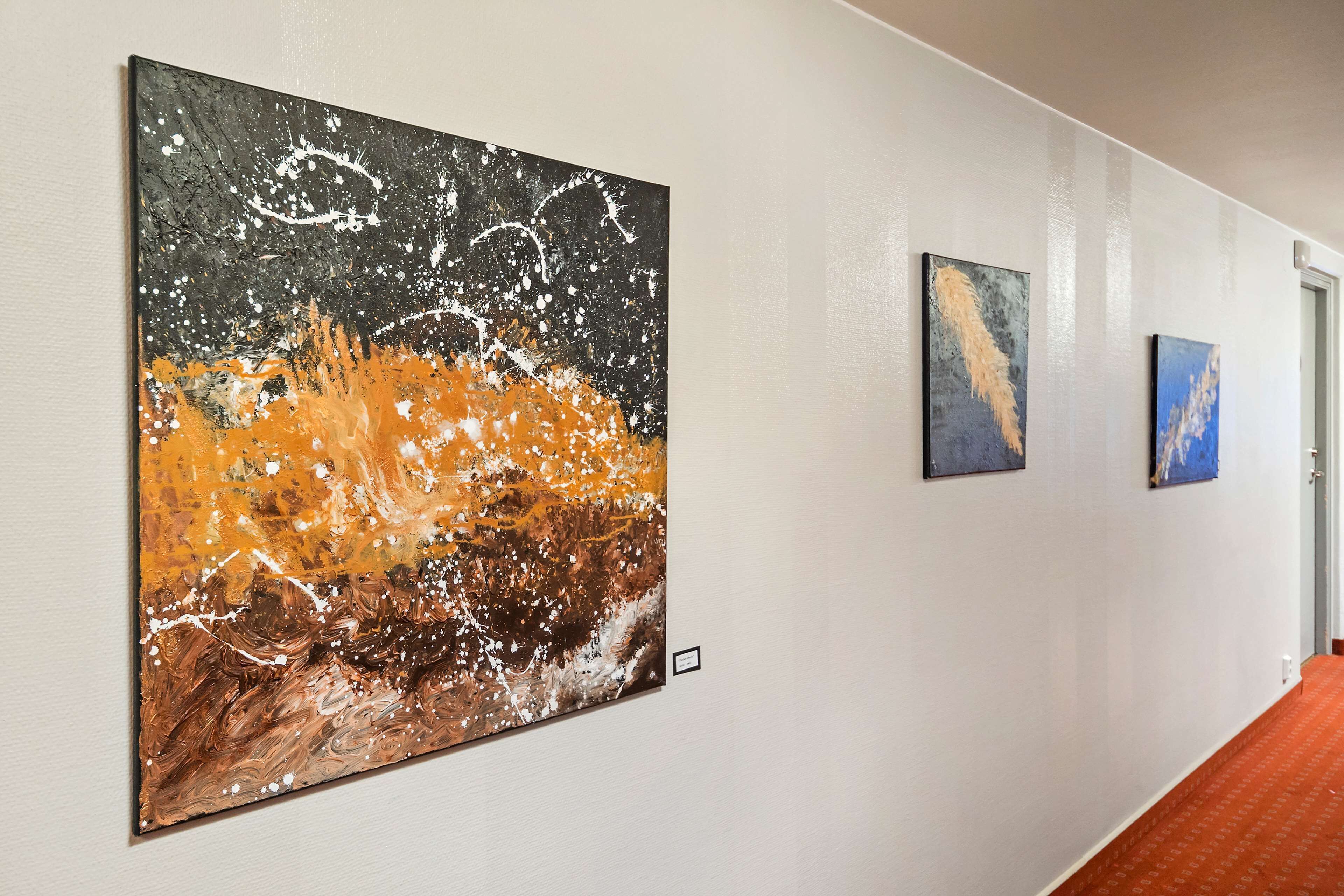 Un couloir dans lequel sont accrochées trois œuvres d’art au mur.