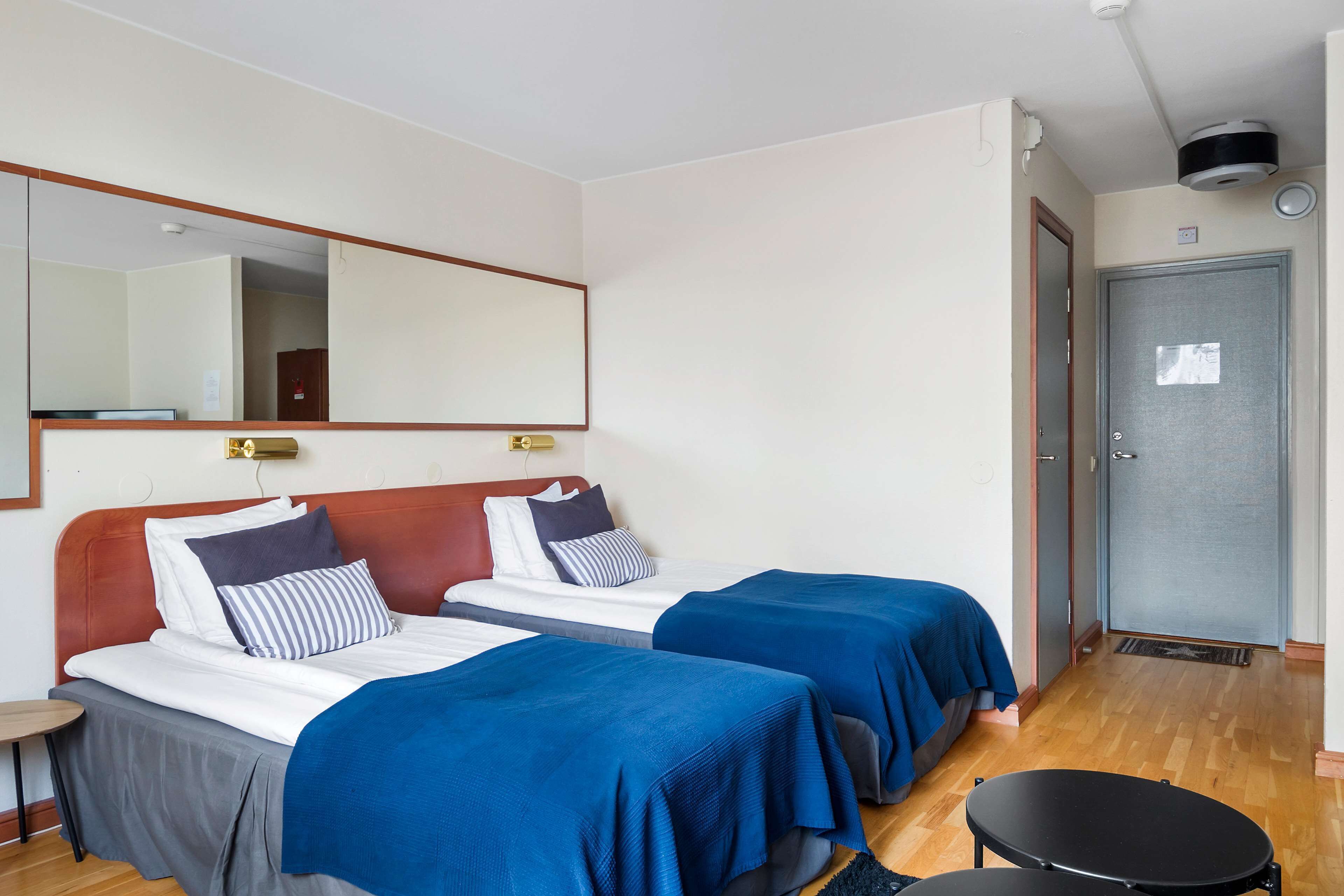 Une chambre d’hôtel avec deux lits, un miroir, une porte et une petite table ronde.