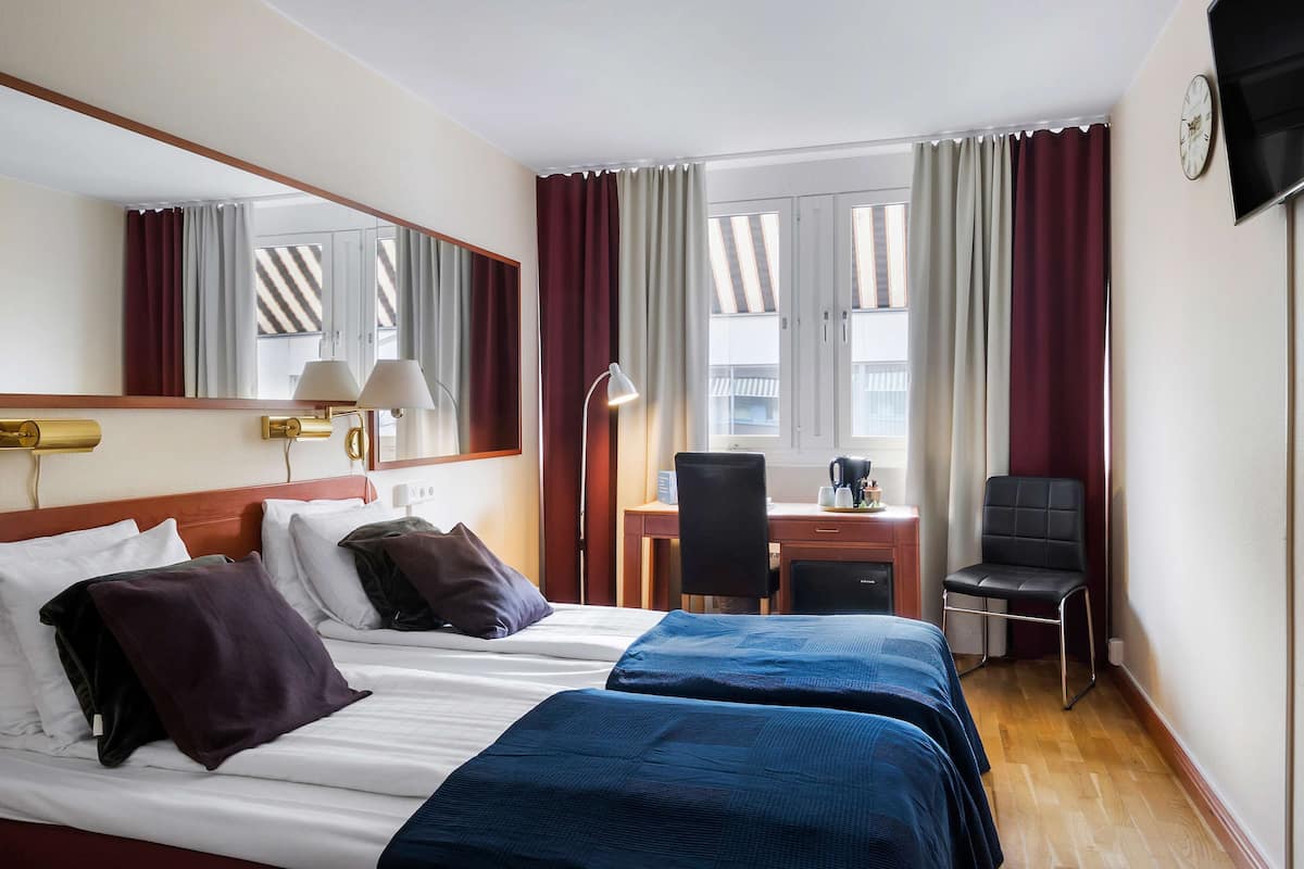 Une chambre d’hôtel avec deux lits, un bureau, une chaise, une télévision et une fenêtre avec des rideaux.