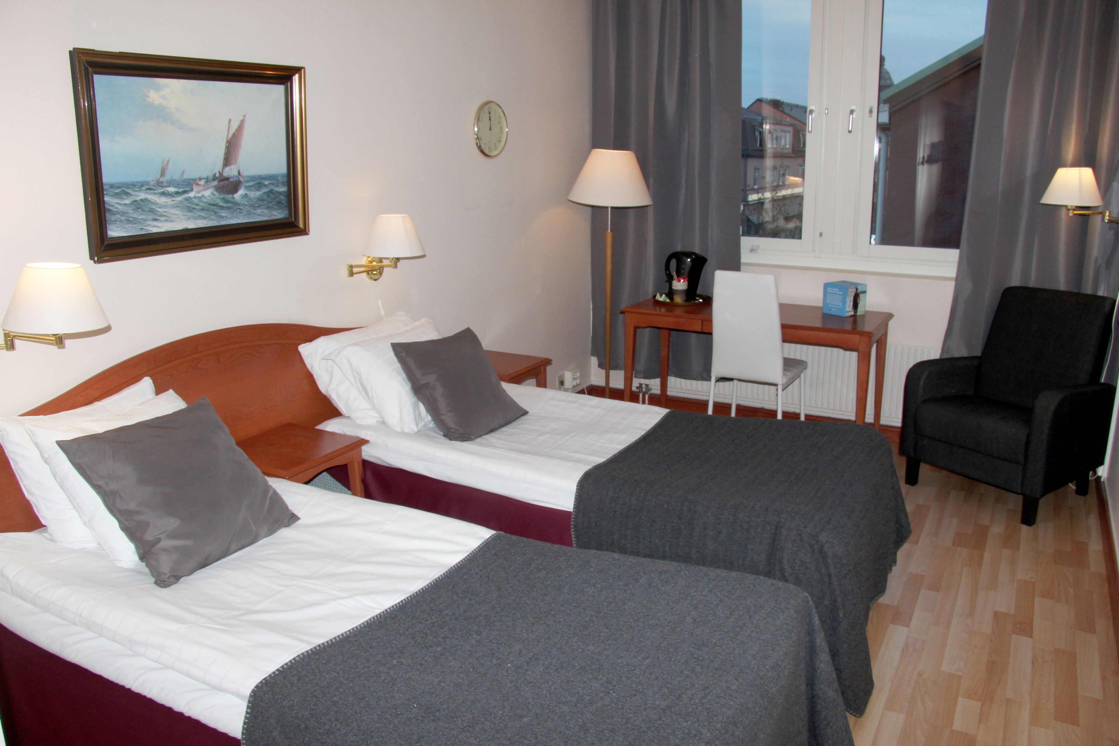 A hotel room with two beds, a desk, a chair, and a window with curtains.