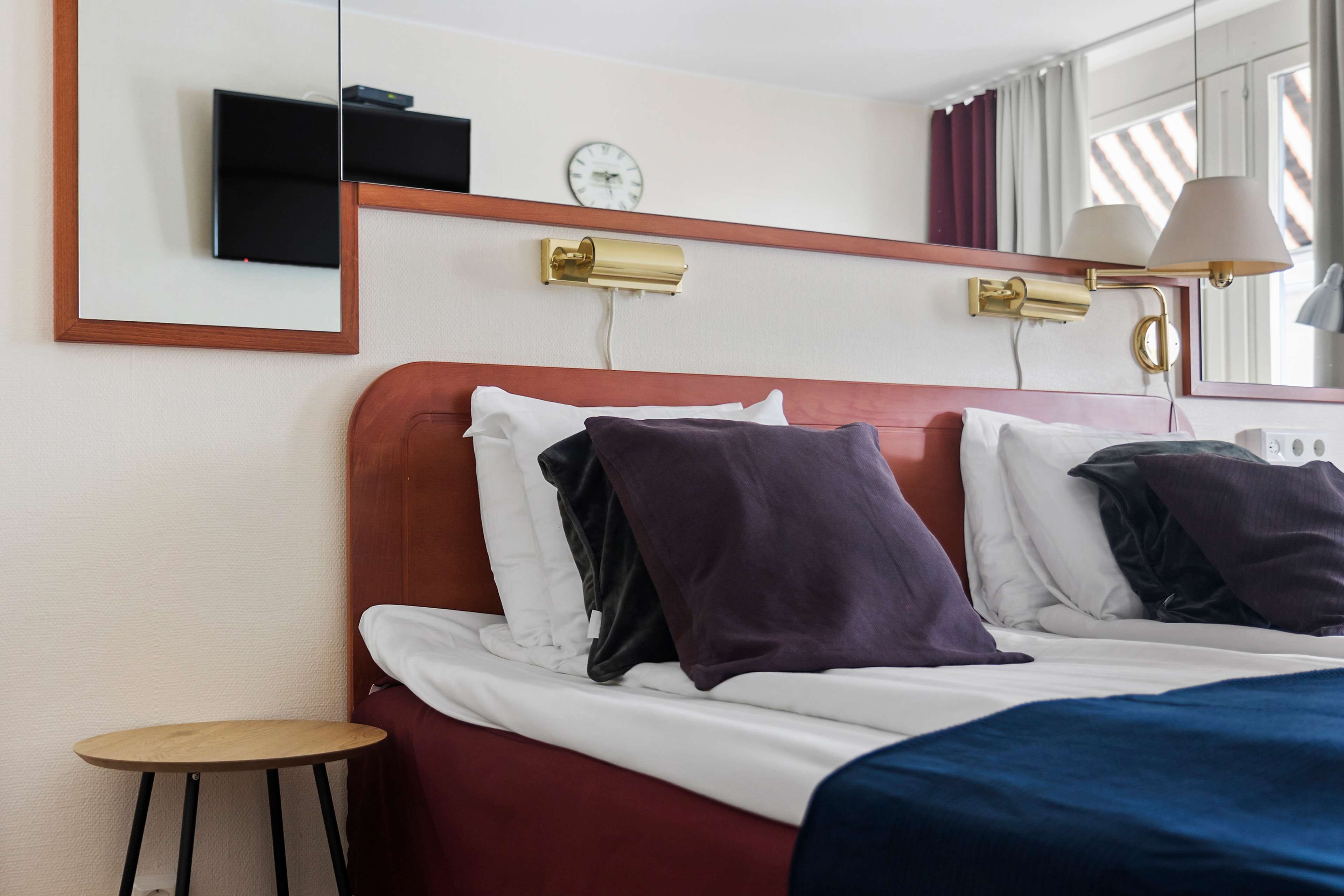 Ein Hotelzimmer mit Bett, einem kleinen Tisch, einer Uhr und einer Lampe.