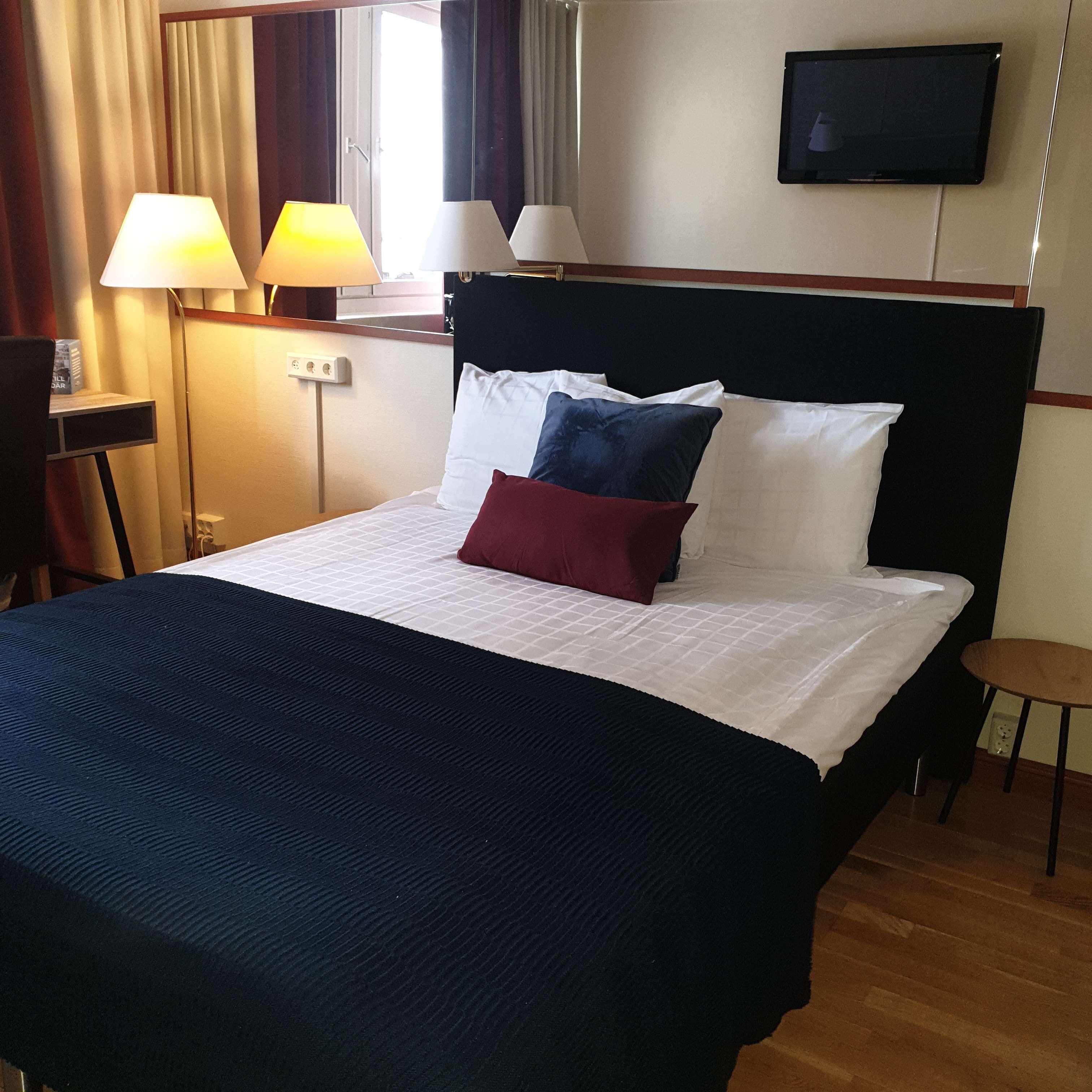 Habitación de hotel con cama, dos lámparas de noche, un televisor en la pared y una mesita.