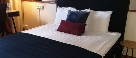 A hotel room with a bed, two bedside lamps, a TV on the wall, and a small table.