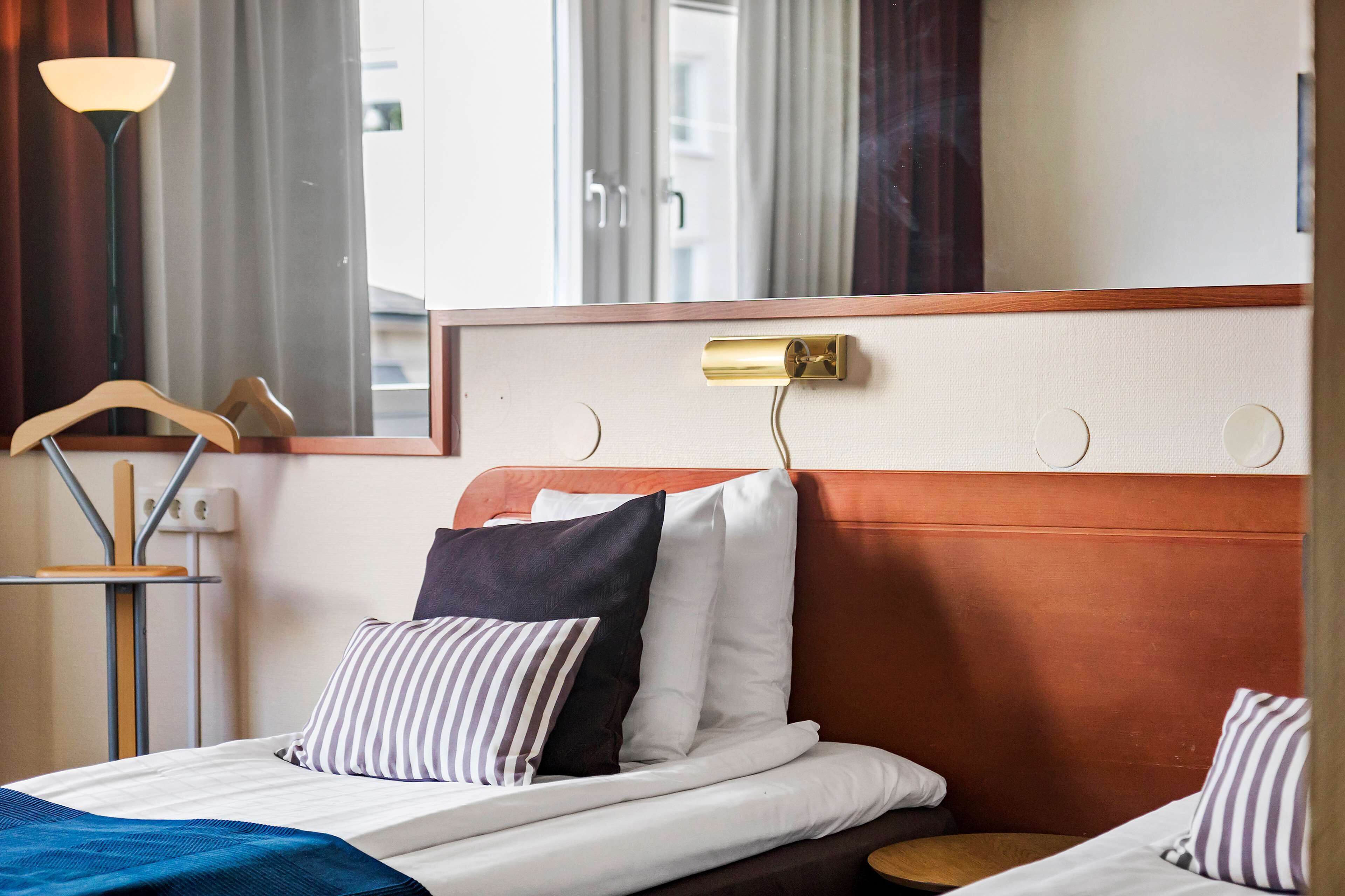 Ein Hotelzimmer mit Bett, Nachttisch, Lampe und Blick nach draußen.