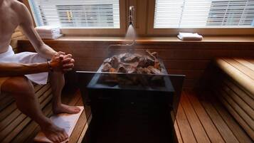 Una sala de sauna con una persona sentada en un banco, una mesa de sauna y una ducha de vapor.