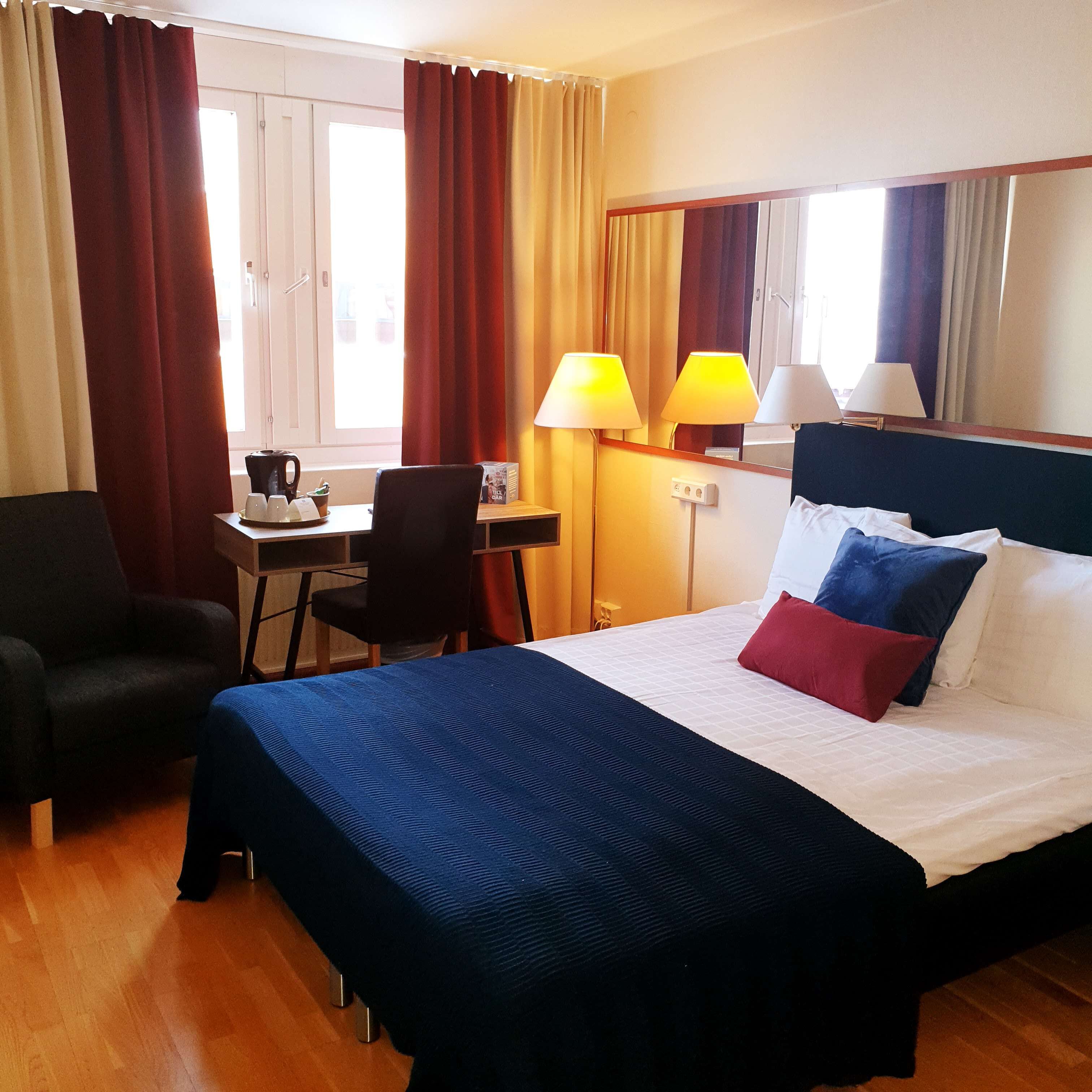 A hotel room with a bed, a desk, a chair, and a window with curtains.