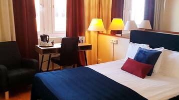 A hotel room with a bed, a desk, a chair, and a window with curtains.