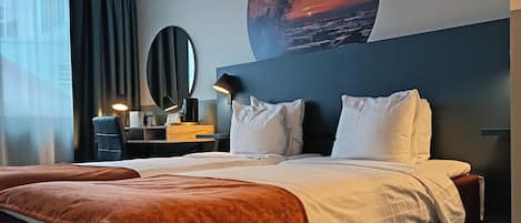 Una habitación de hotel con una cama grande, un escritorio con lámpara, un espejo redondo y una pared con una pintura de atardecer.