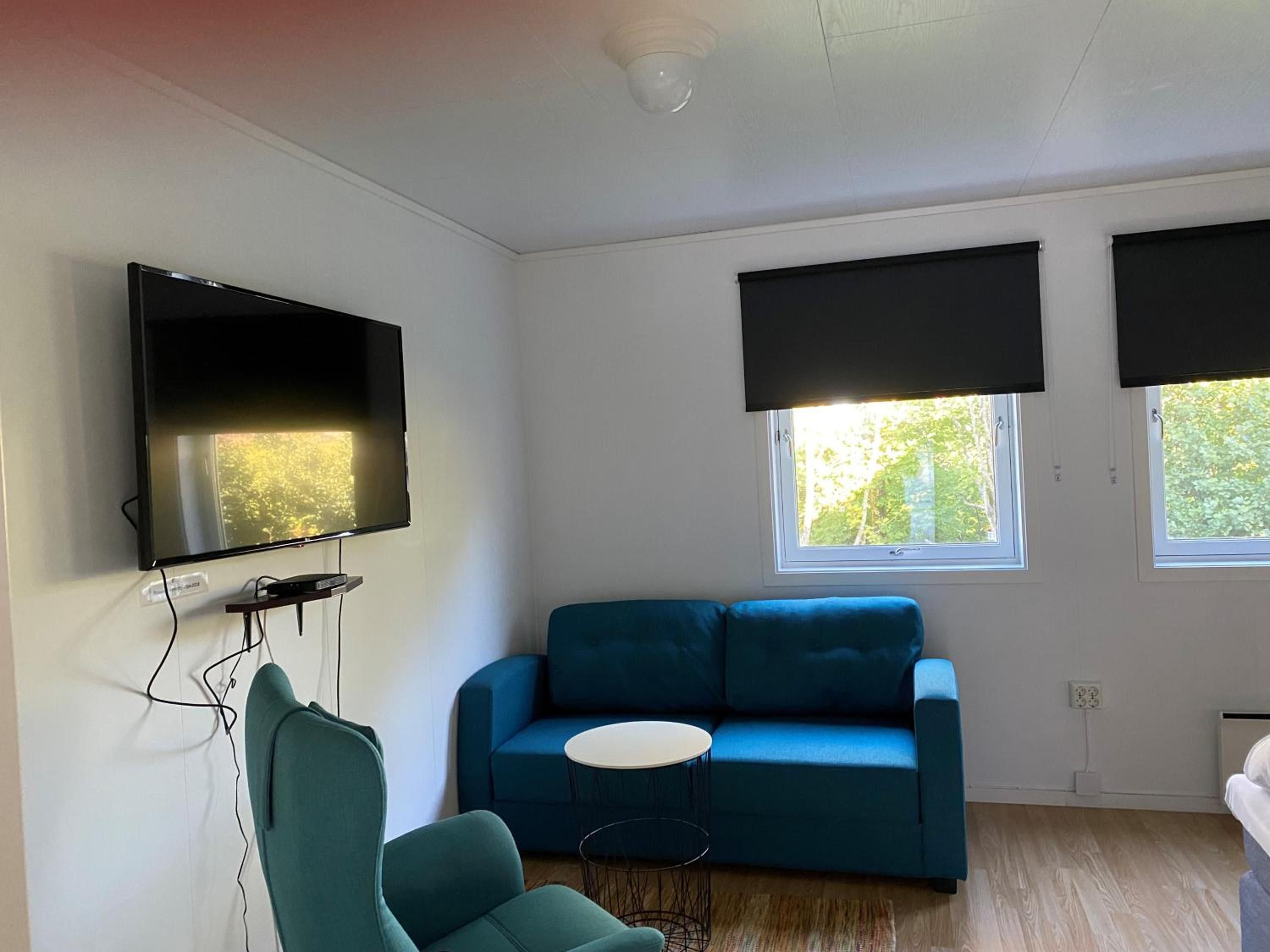 A modern living room with a flat-screen TV, a blue sofa, a small round table, and a teal armchair.