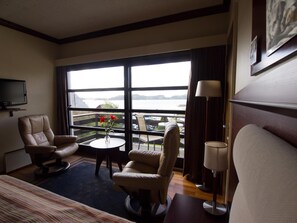 A hotel room with a large window, a television, a bed, two chairs, a small table with flowers, and a lamp. - Fitjar Fjord Hotel (Fitjar)
