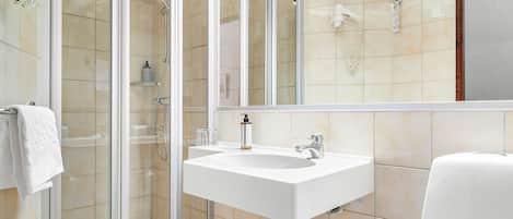 Un baño moderno con ducha de vidrio, lavamanos blanco y un espejo grande.