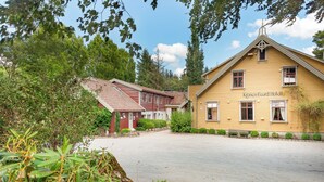 A hotel with a red and yellow facade, a paved courtyard, and surrounding greenery. - Kronen Gaard Hotel (Sandnes)