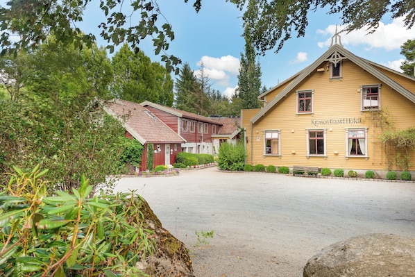 A hotel with a red and yellow facade, a paved courtyard, and surrounding greenery. - Kronen Gaard Hotel (Sandnes)