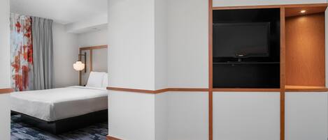 A hotel room with a bed, a television, and a wall-mounted light fixture.