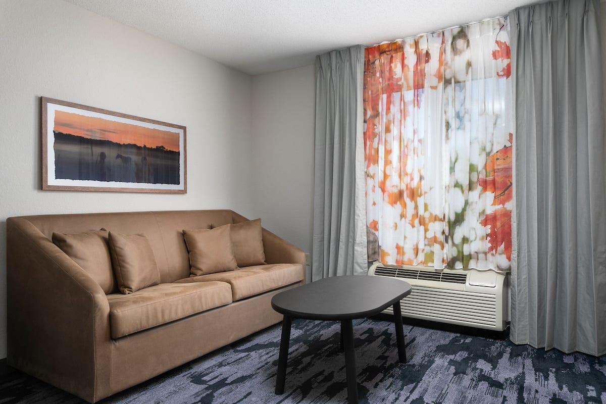 A modern living room with a beige sofa, a small table, and a large window with floral curtains.