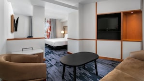 Quarto de hotel com uma cama, uma escrivaninha, uma TV e um sofá.
