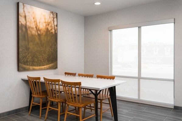 Un comedor con una mesa blanca y sillas de madera, un cuadro abstracto grande en la pared y un ventanal con vistas a edificios.