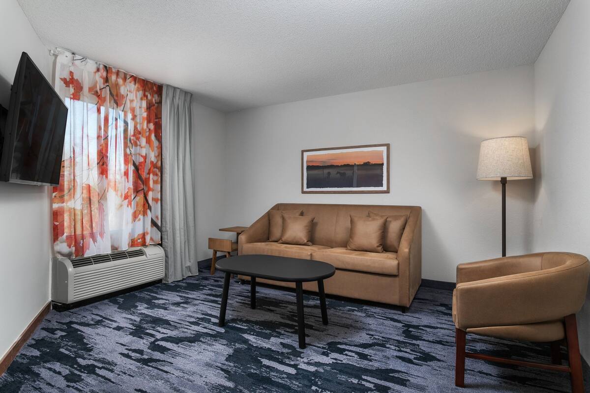 A hotel room with a sofa, a chair, a small table, a TV, a lamp, and a painting on the wall.