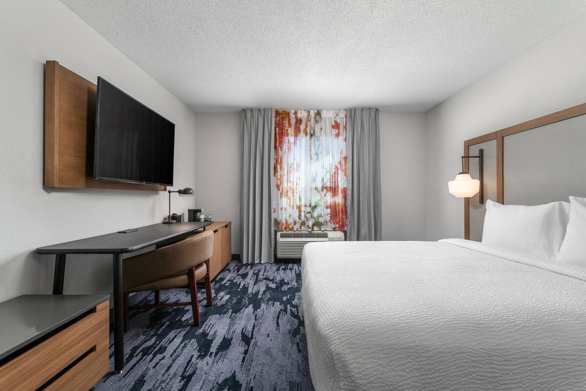 A hotel room with a bed, desk, chair, TV, and a window with curtains.