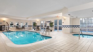 Piscina interior com chão em azulejo, sala de trocas e área de estar com cadeiras.