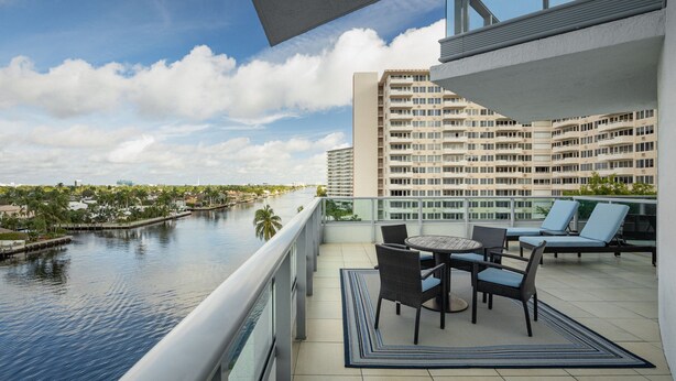 Un balcon donnant sur une rivière, une table à manger avec des chaises et une rambarde.