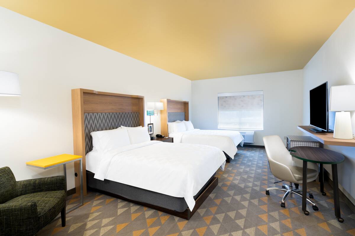 Une chambre d’hôtel avec deux lits, un bureau, une chaise et une télévision.