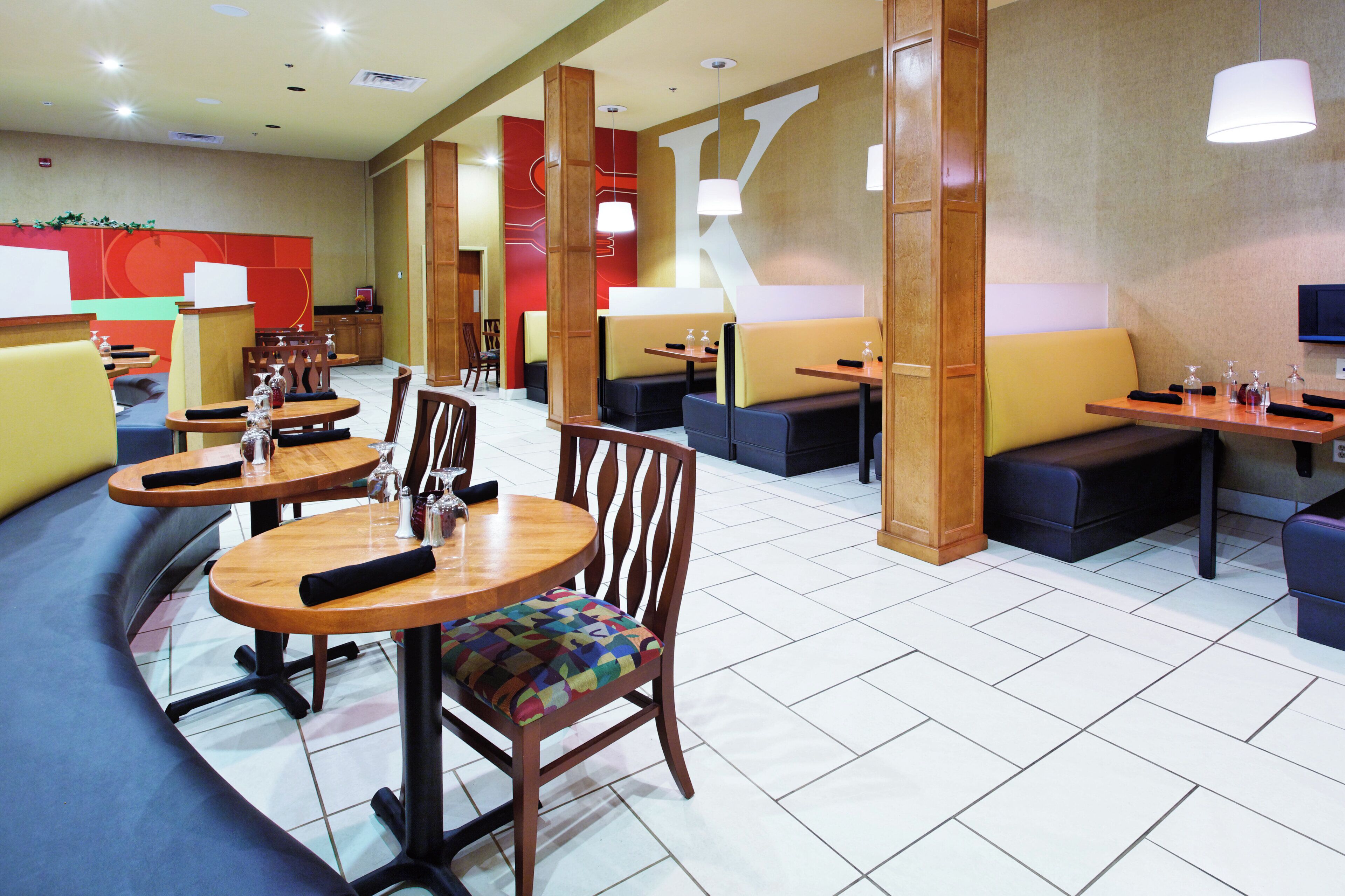 A hotel dining area with round tables, cushioned seating, and pendant lighting.