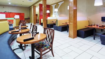 A hotel dining area with round tables, cushioned seating, and pendant lighting.