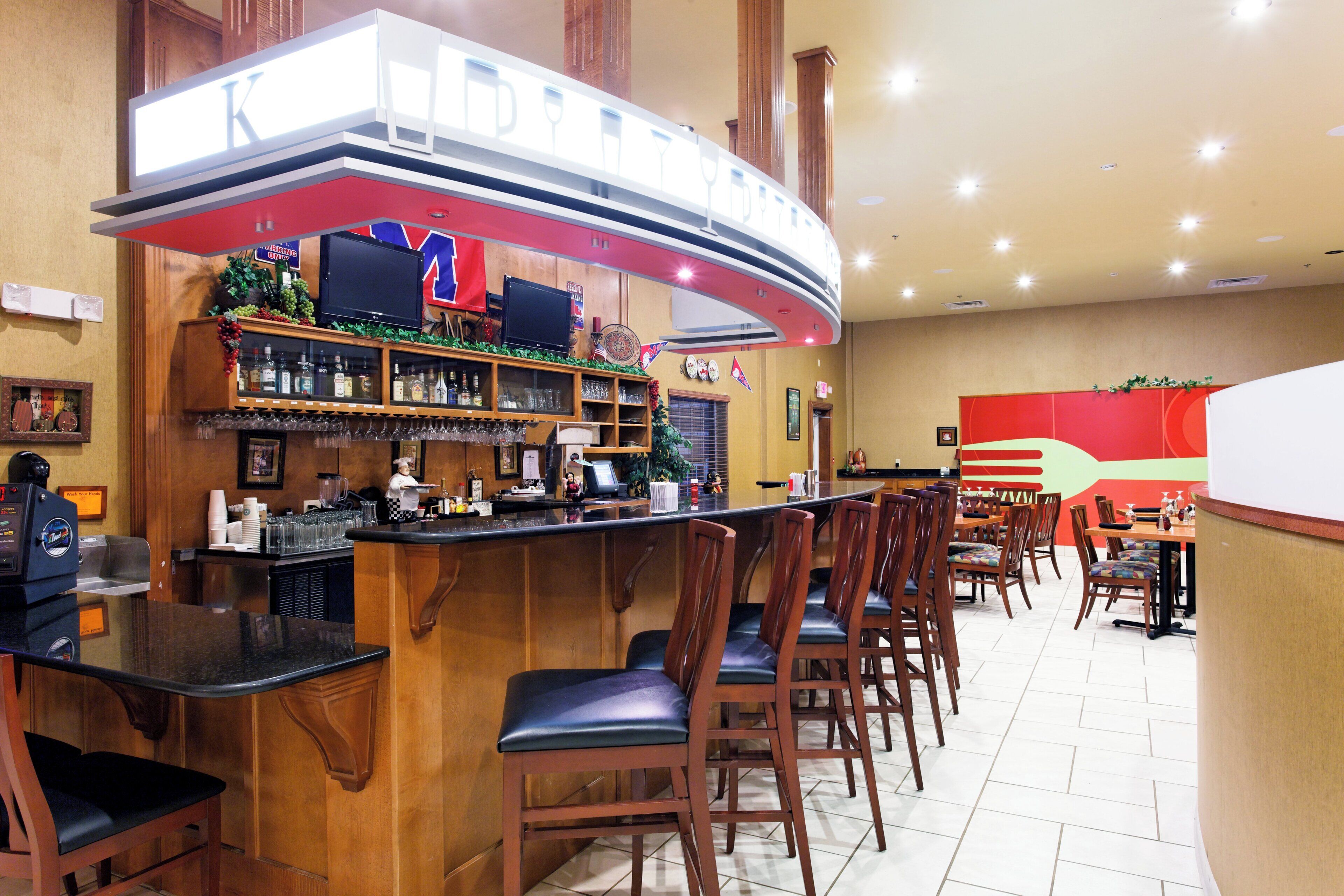 A bar area with a curved counter, bar stools, and a television screen.
