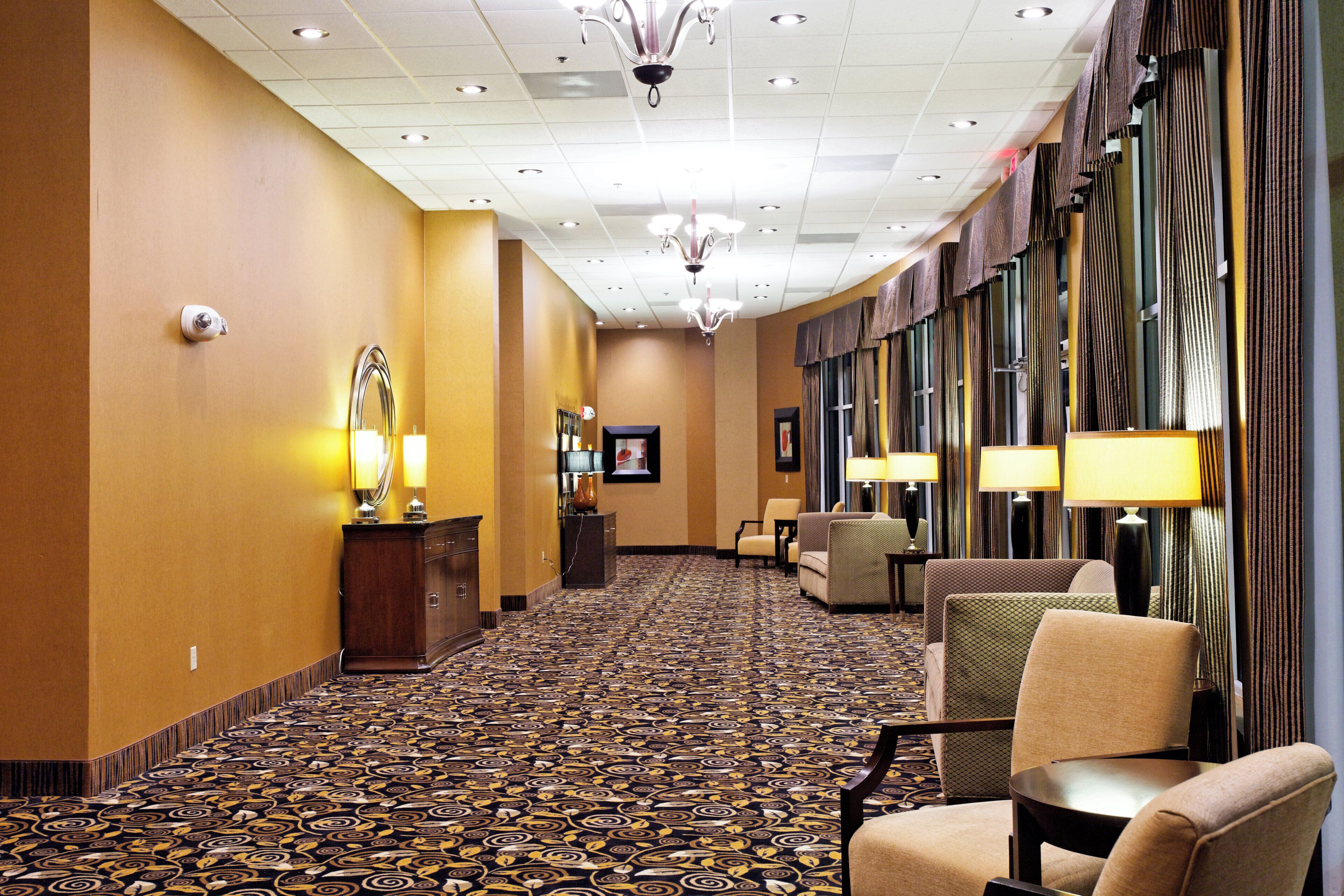 A hotel corridor with patterned carpet, seating areas, and a chandelier.