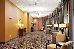 A hotel corridor with patterned carpet, seating areas, and a chandelier. - Holiday Inn Batesville by IHG (Batesville)